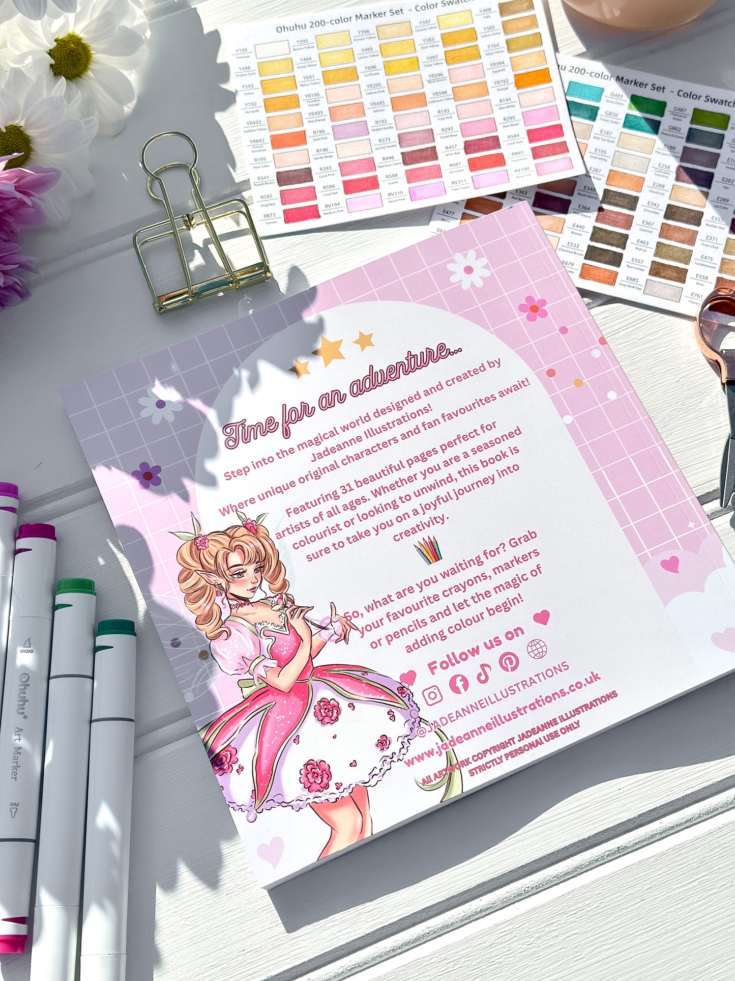 Colour swatches, markers, and a colouring book page with an illustration of a fairy on a white surface.