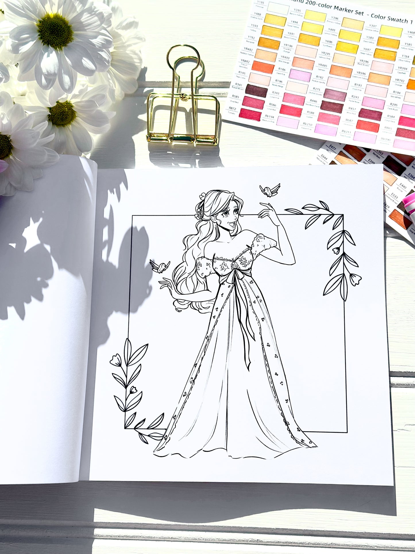 Colouring book page with a woman in a dress and flowers, surrounded by markers and a colour swatch.