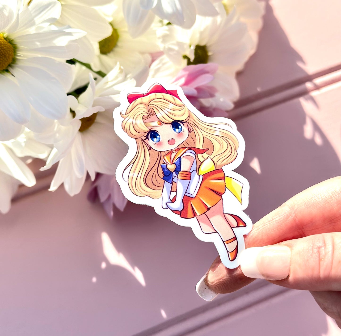 Sticker of Sailor Venus character held by a hand with white flowers in the background