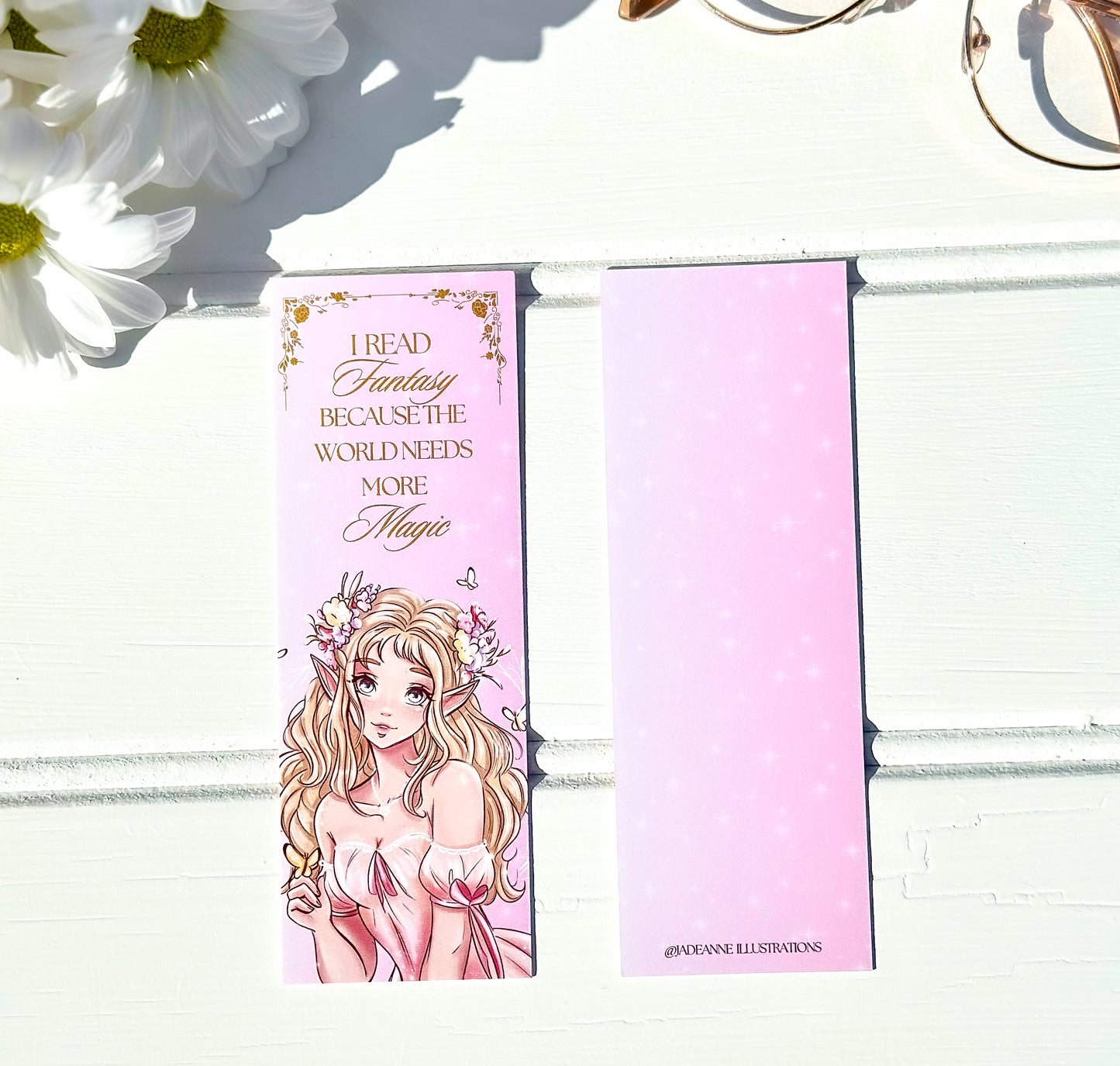 Pink bookmark with an illustration of a fairy princess and text on a white wooden surface with flowers.