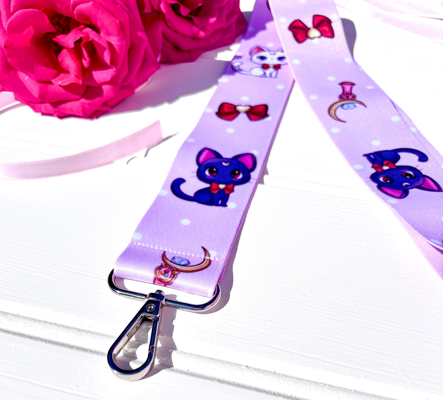 Lanyard with sailor moon cat design on a white surface with pink flowers.