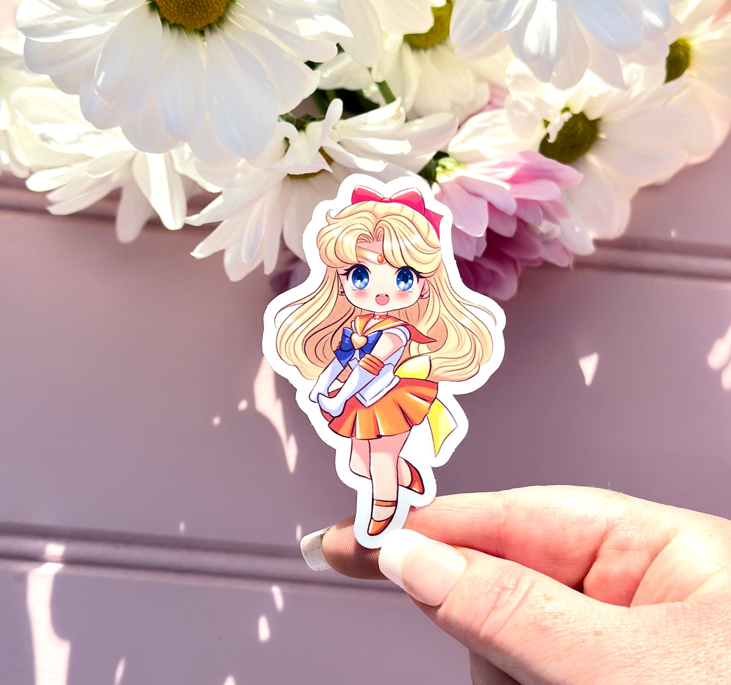 Sticker of a Sailor Venus character held by a hand with flowers in the background