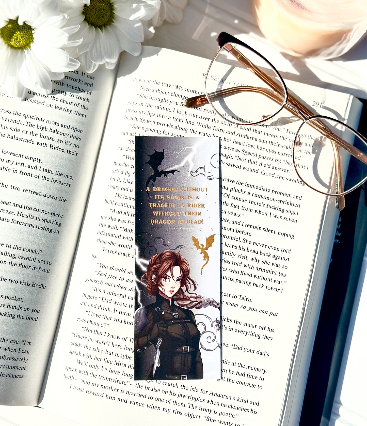 Book with a bookmark featuring an illustration of Violet sorrengail ,glasses, and flowers on an open book.