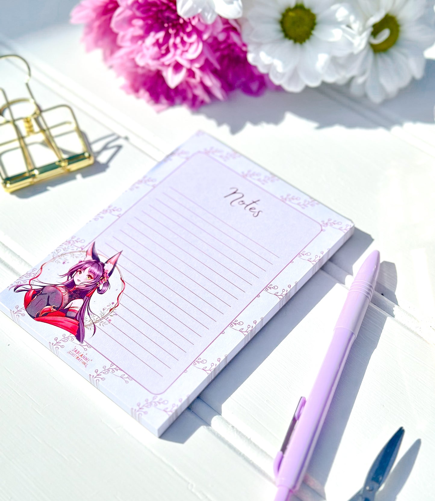 Notepad with anime fox character design, pen, and flowers on a light surface