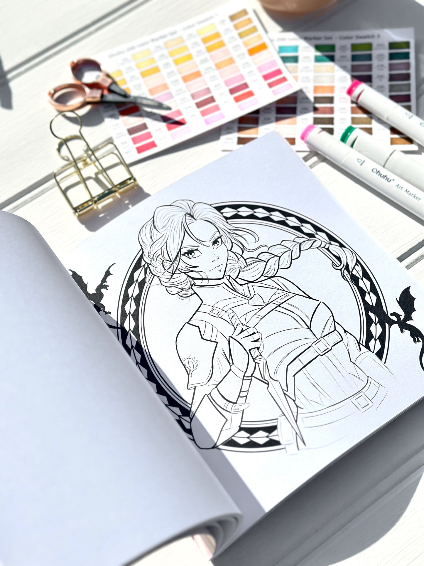 Colouring book with a completed illustration of a character, surrounded by art supplies including scissors and colour swatches.