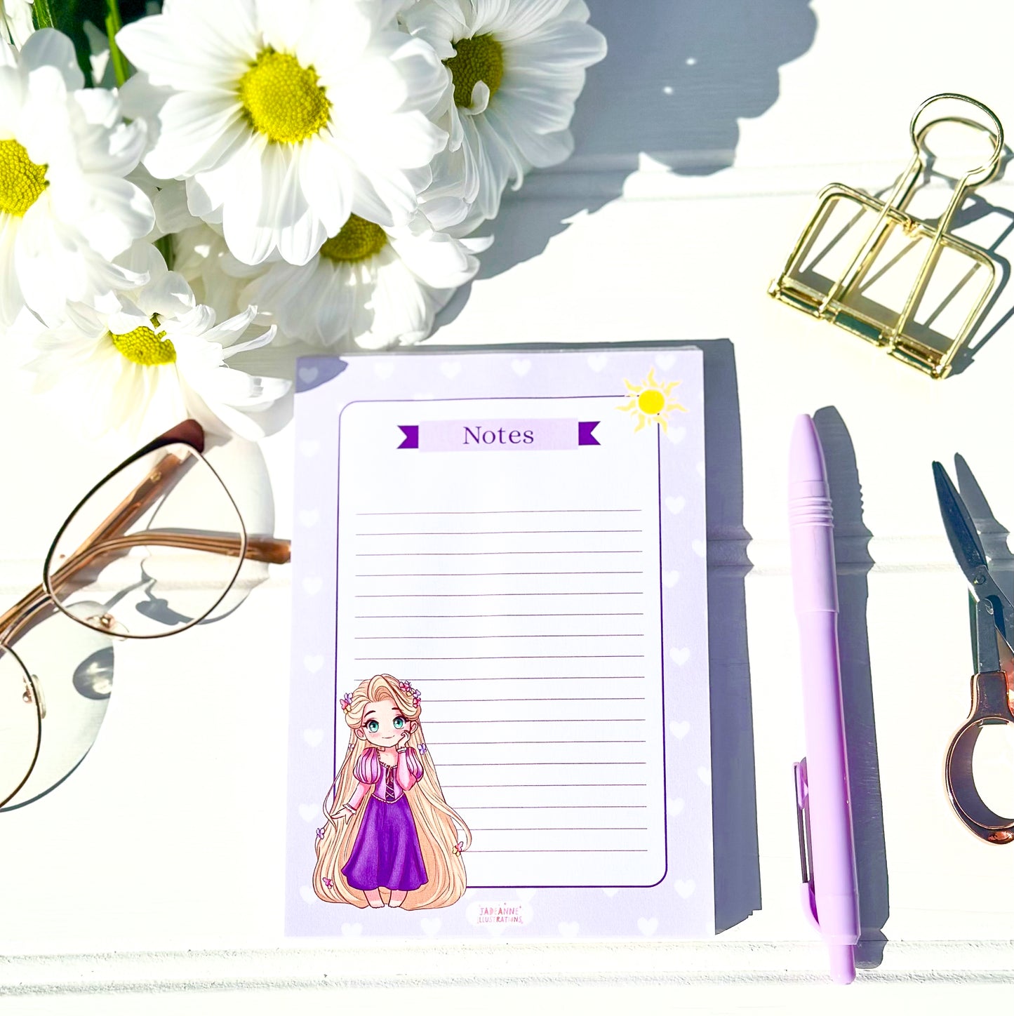 Notepad with Chibi rapunzel character, pen, scissors, glasses, and flowers on a white surface