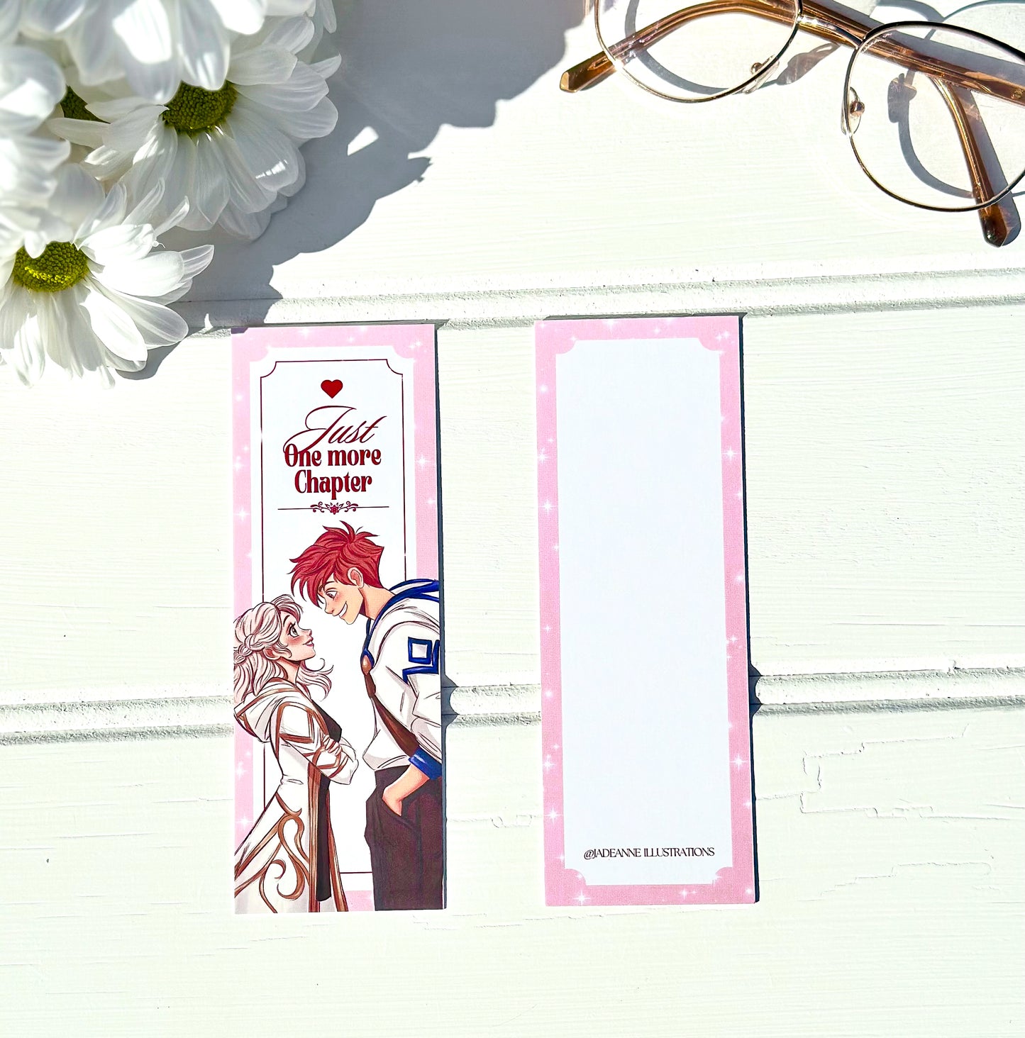 Anime-style bookmarks with couple illustration and text on a white surface with flowers and glasses.