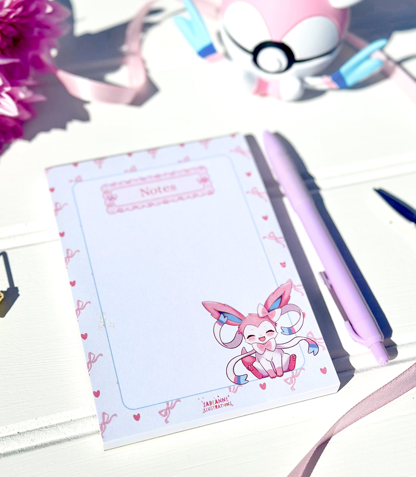 Notebook with a cute pokemon sylveon character design on a white surface with a pen and flowers.