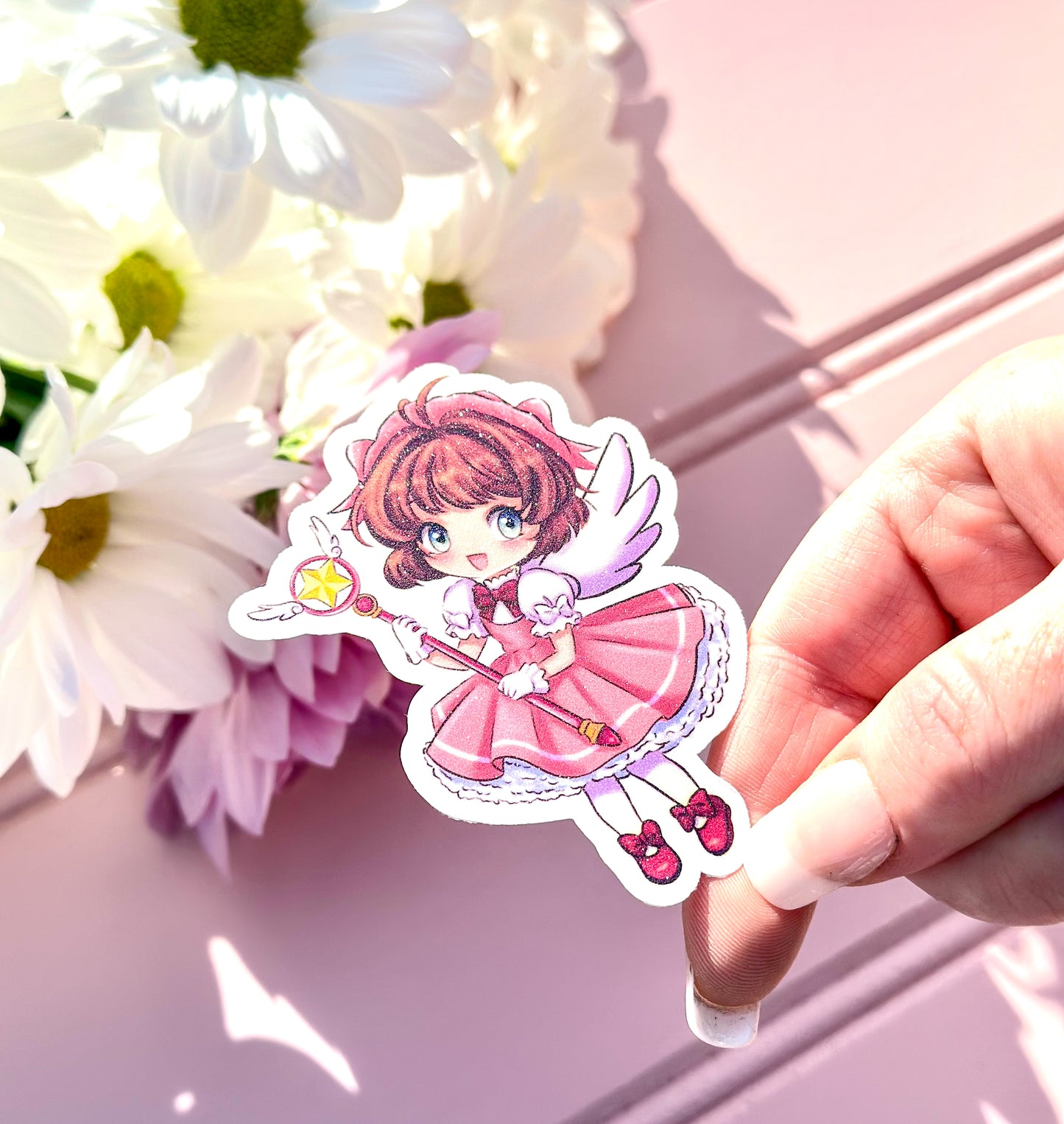 Hand holding a vinyl sticker of an anime character sakura with flowers in the background
