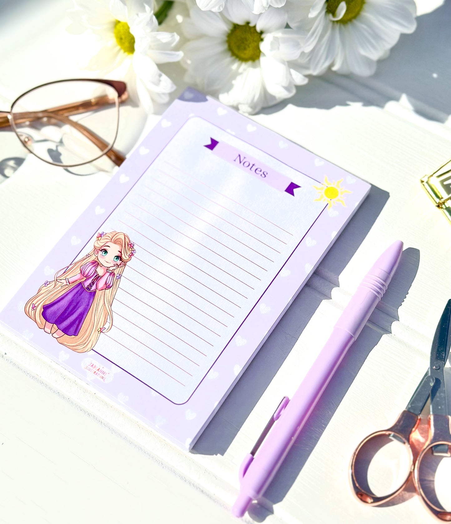 Notepad with kawaii princess character, pen, scissors, and glasses on a light surface with flowers.