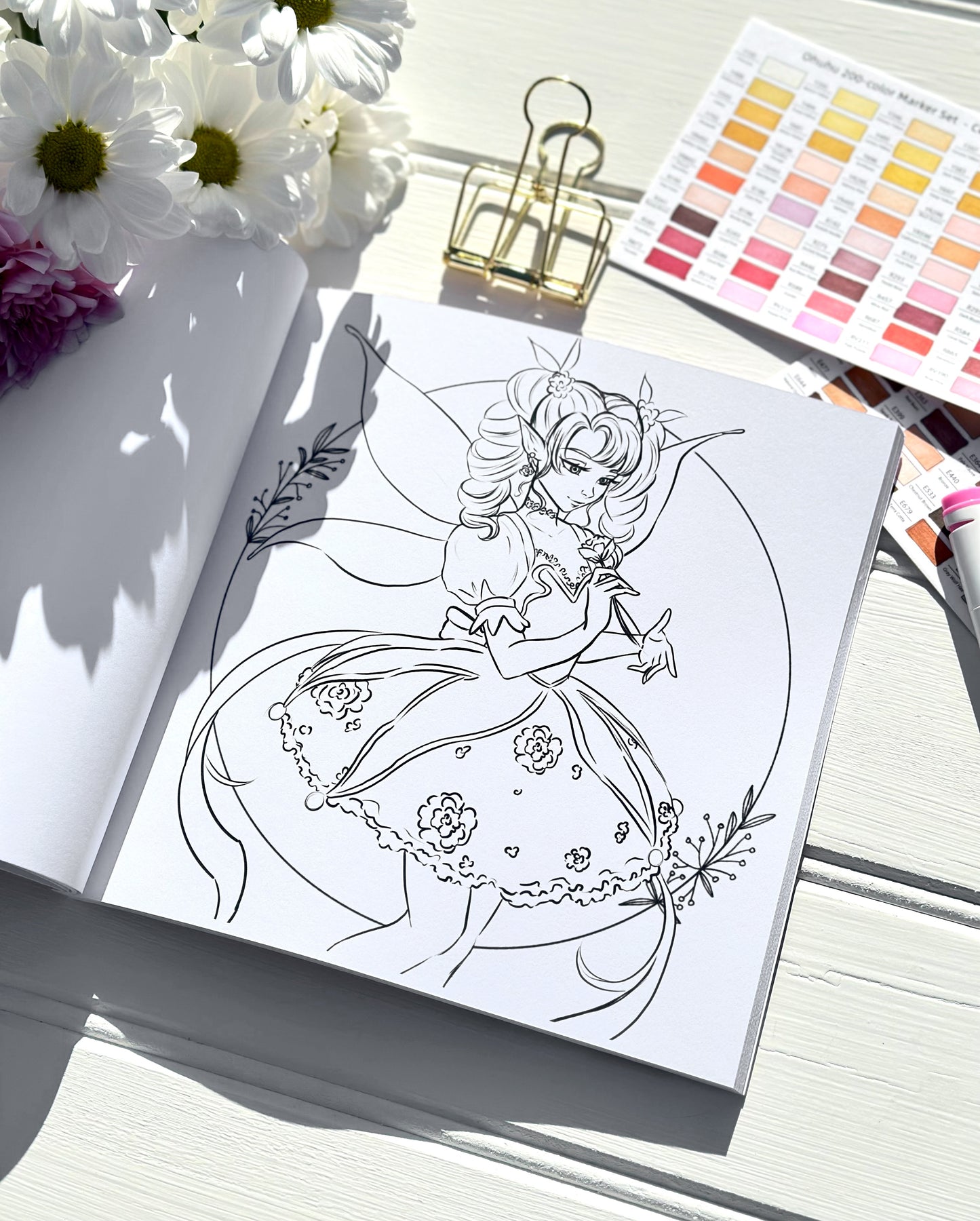 Colouring book page with a fairy design, flowers, and colour swatches on a white surface.