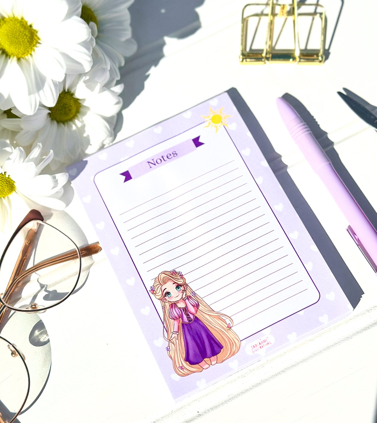 Notepad with princess rapunzel character, pen, glasses, and flowers on a white surface