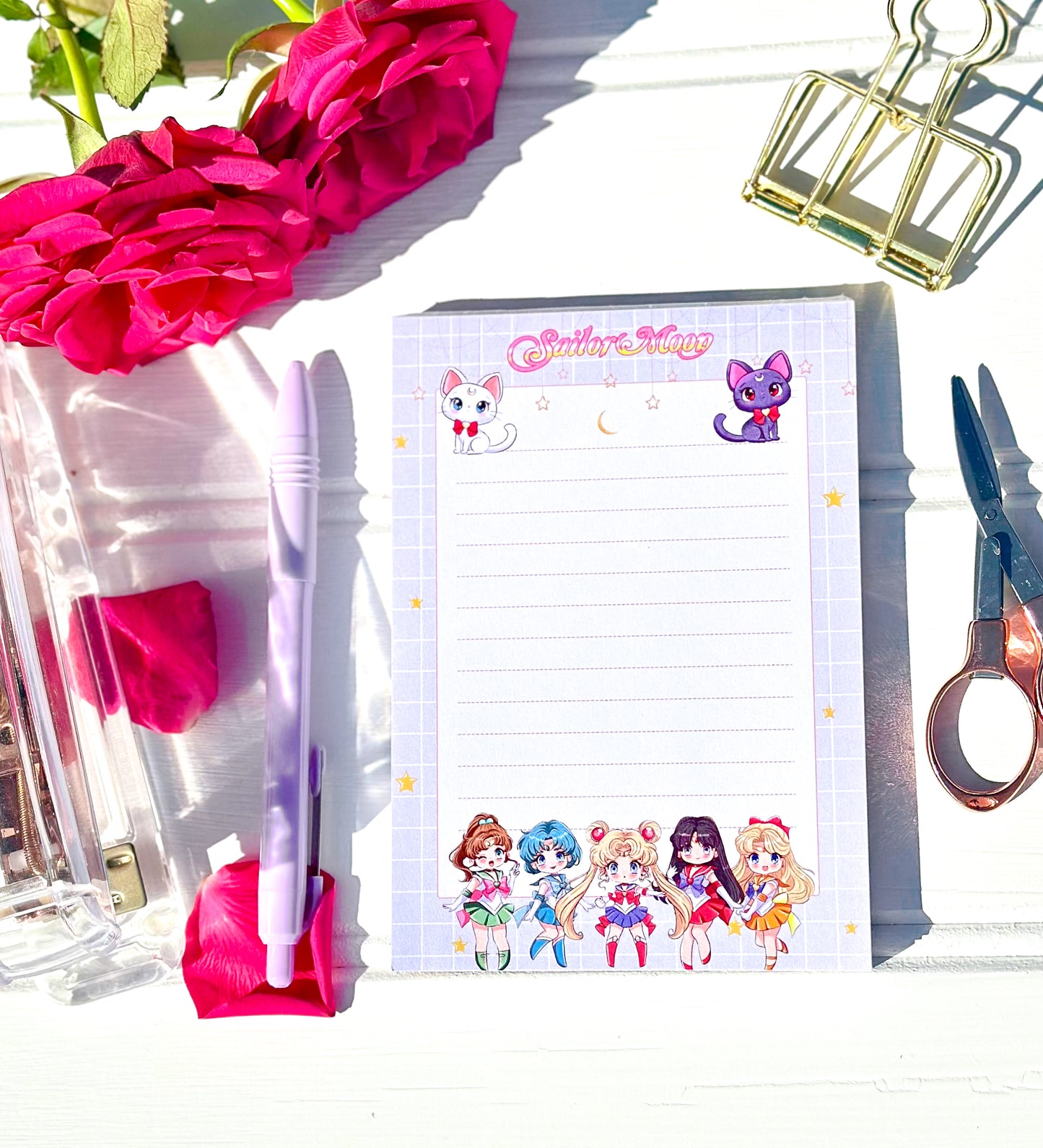 Notepad with sailor moon characters design, pen, and stationery items on a white surface