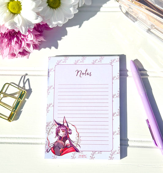 Notepad with anime character design on a white surface with flowers and a pen.