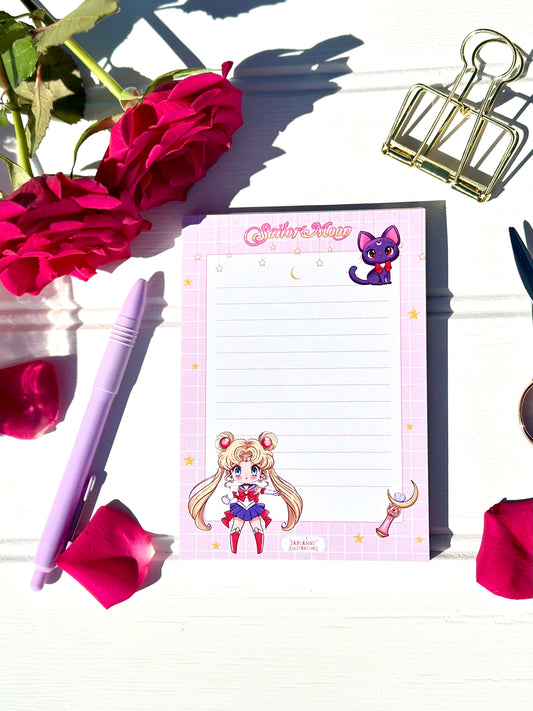 Sailor Moon-themed notepad with a pen and flowers on a white surface