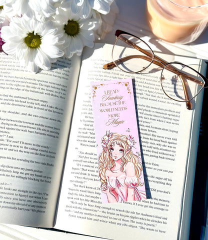 Open book with a pink bookmark featuring an illustration of a fairy princess, glasses, and flowers on a white surface.