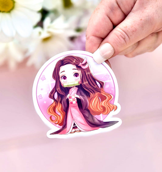Sticker of nezuko from demon slayer with long hair held by a hand against a blurred floral background