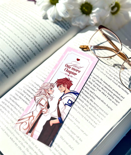 Book with an anime-style romantic fantasy couple bookmark featuring two characters, glasses, and flowers on an open book.