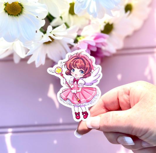 Hand holding a sticker of an anime character sakura from cardcaptors with flowers in the background