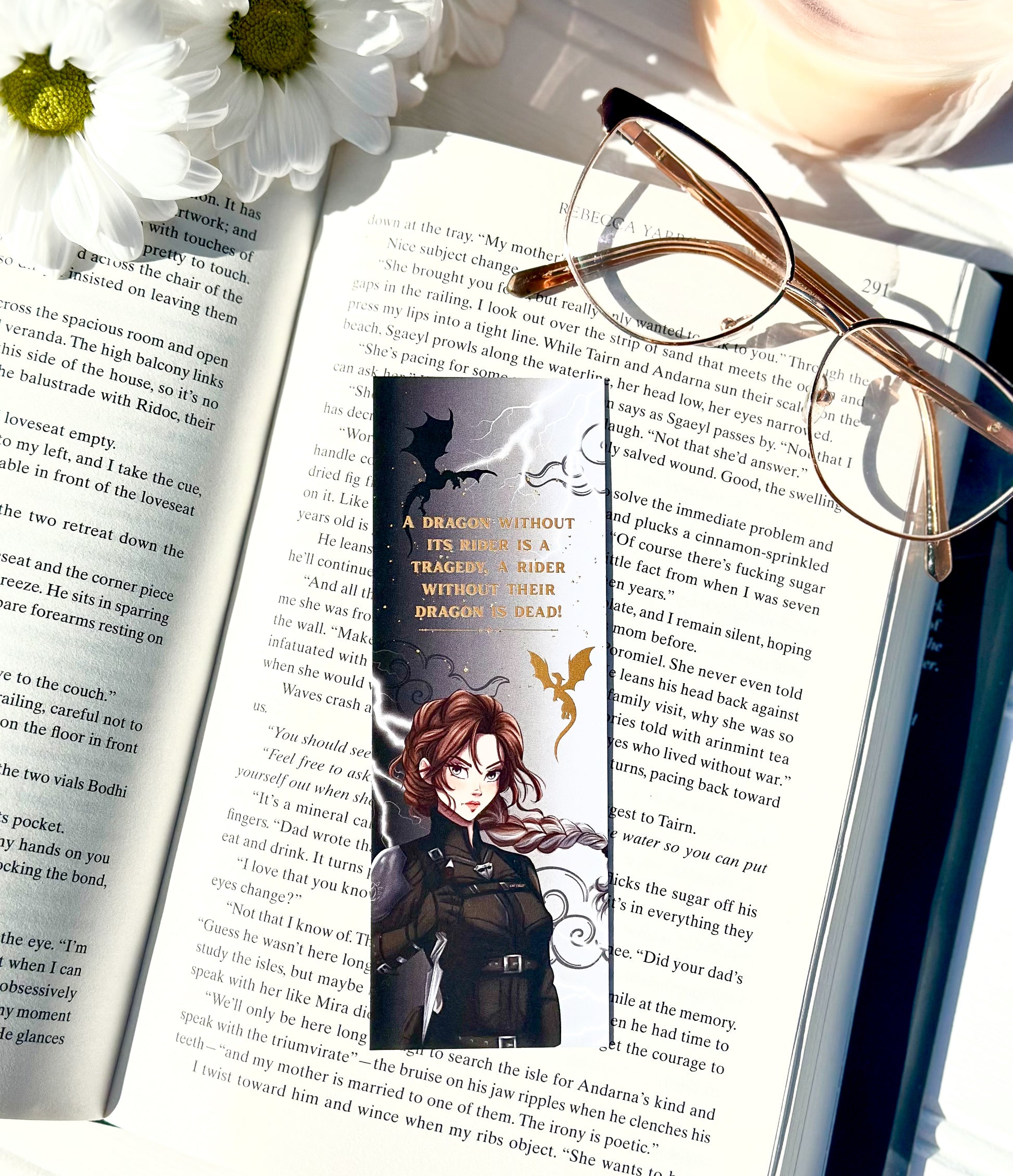 Book with a bookmark featuring an illustration of Violet sorrengail ,glasses, and flowers on an open book.