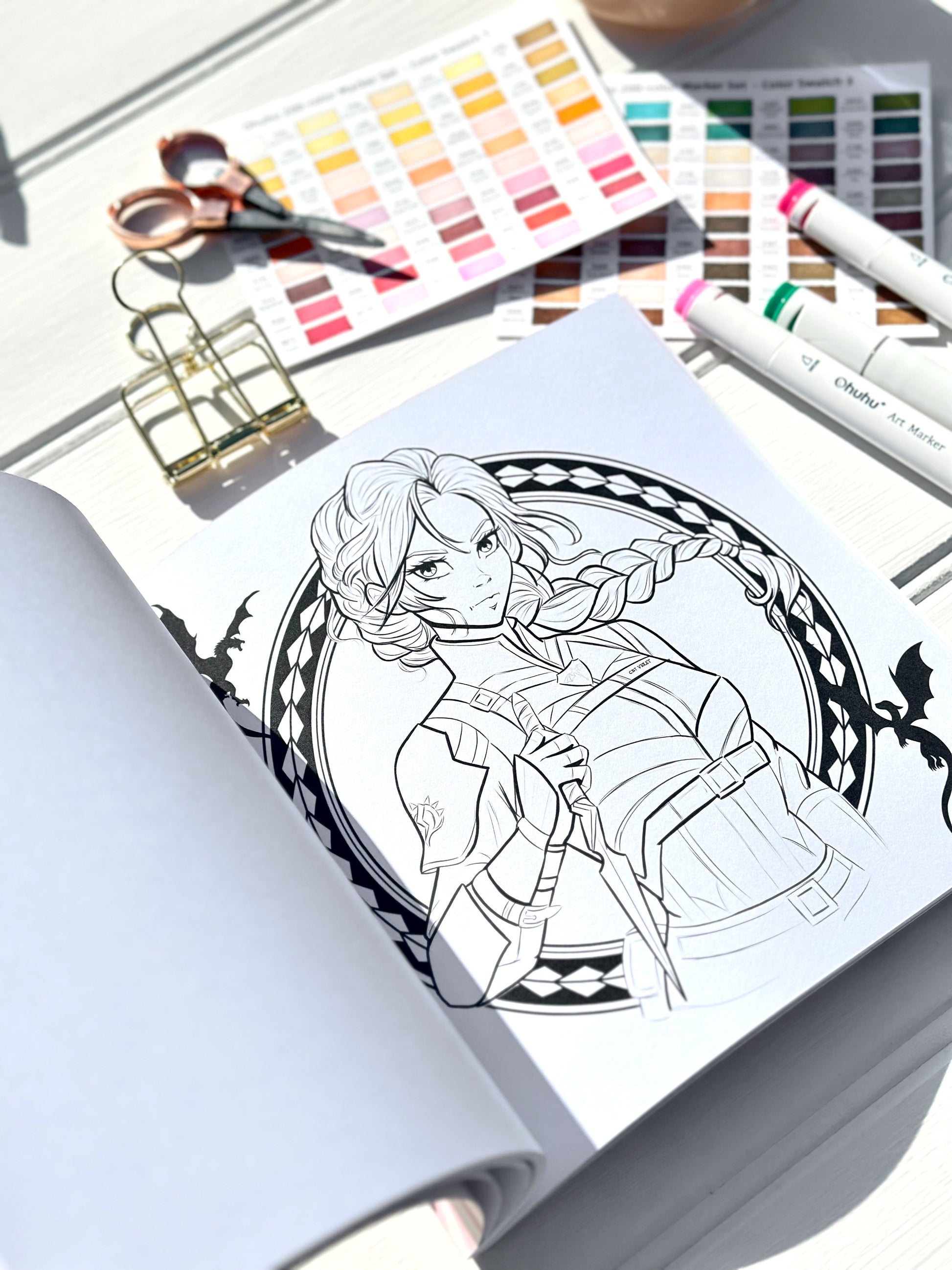 Colouring book with a completed illustration of a character, surrounded by art supplies including scissors and colour swatches.