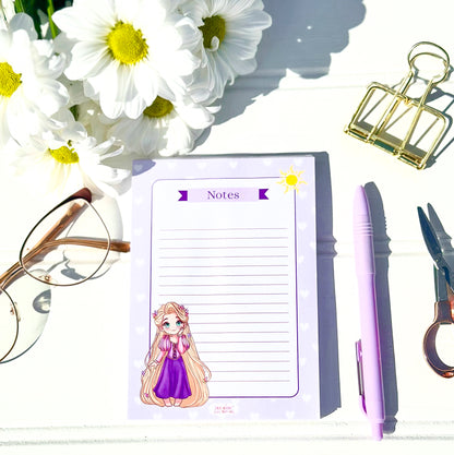 Notepad with Chibi rapunzel character, pen, scissors, glasses, and flowers on a white surface
