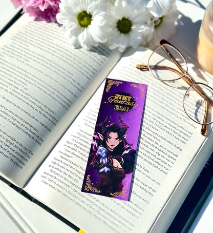 Open book with a purple bookmark featuring a dark fae character, surrounded by flowers and glasses.