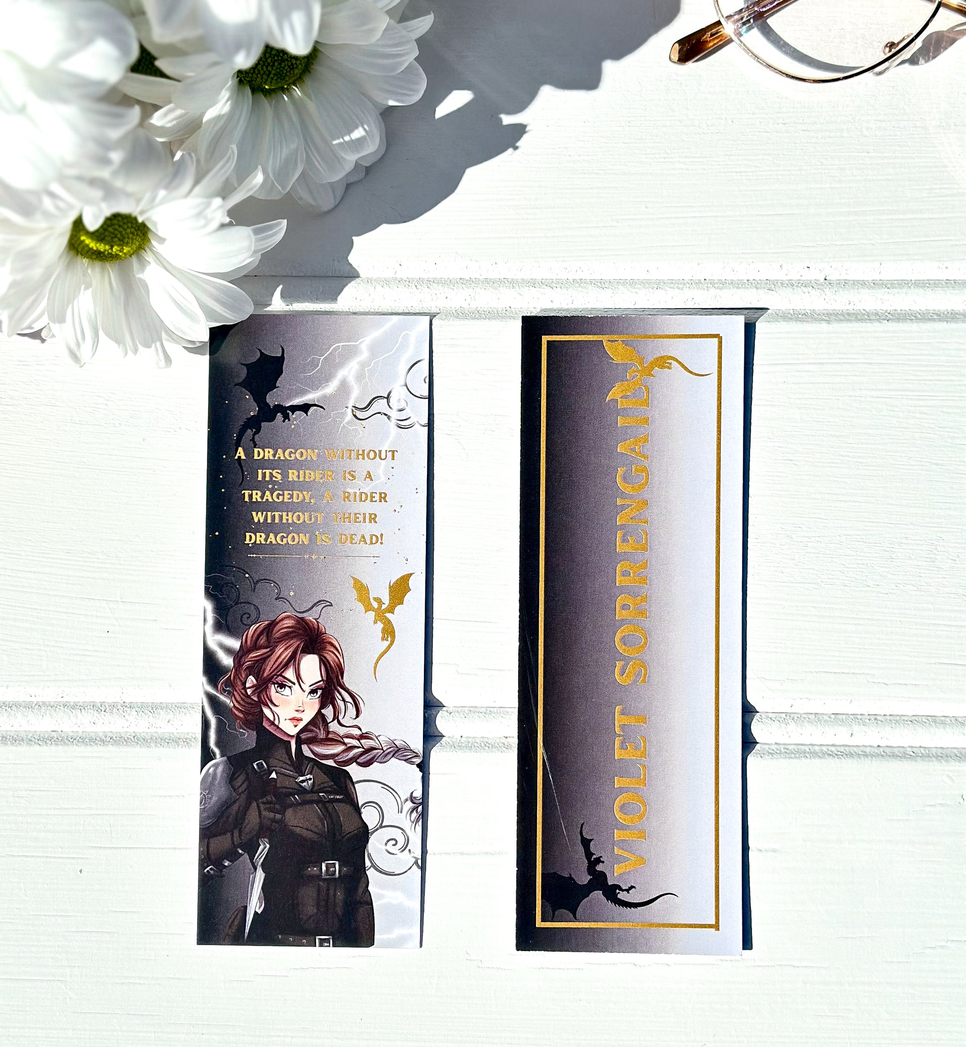 Bookmarks with Violet sorrengail from fourth wing and text on a white surface with flowers and glasses.