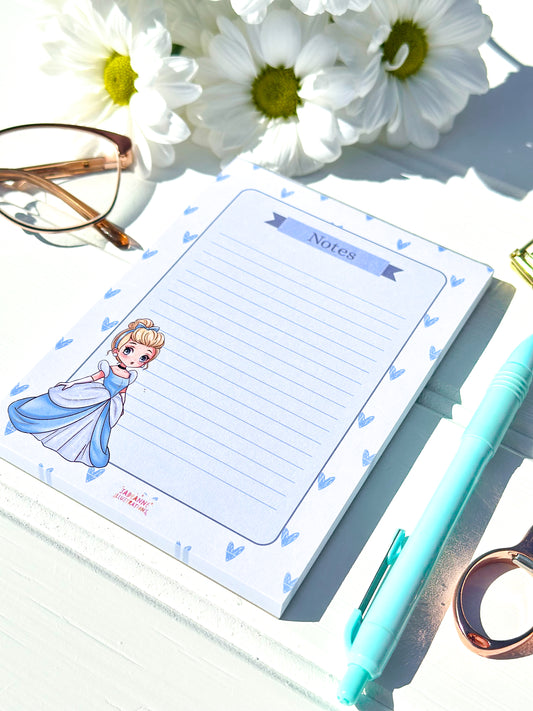 Notepad with a princess cinderella design, pen, and flowers on a white surface