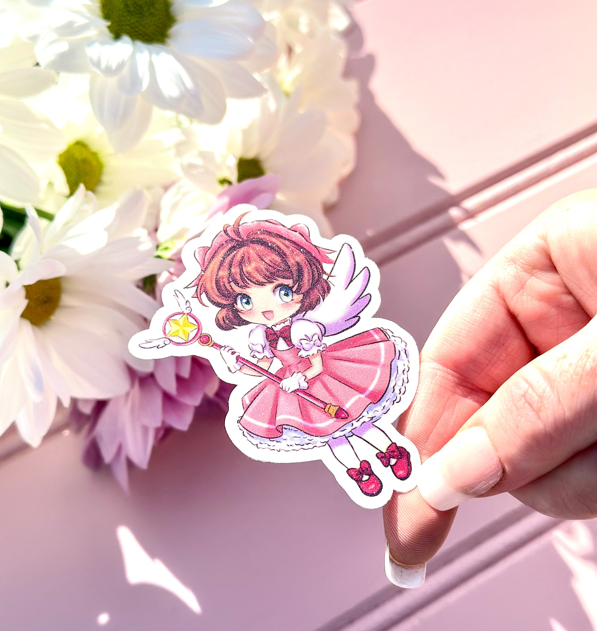Hand holding a vinyl sticker of an anime character sakura with flowers in the background