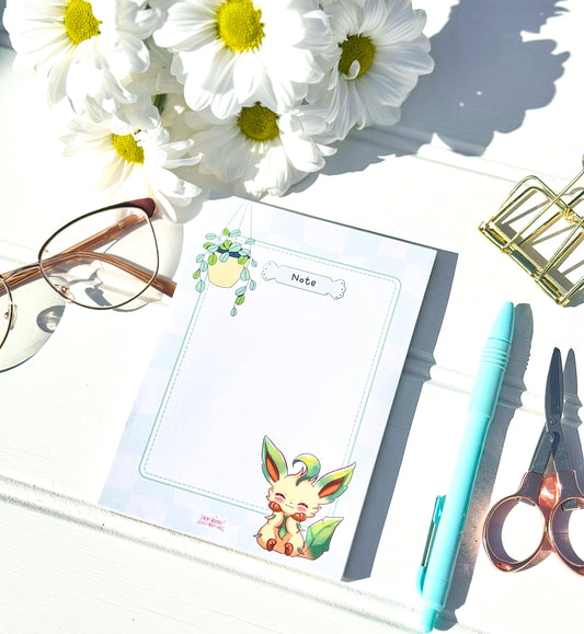 Notebook with cute leafeon pokemon illustrations, glasses, pen, scissors, and flowers on a white surface