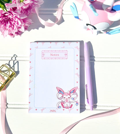 Notebook with kawaii pokemon character design, pen, and flowers on a white background