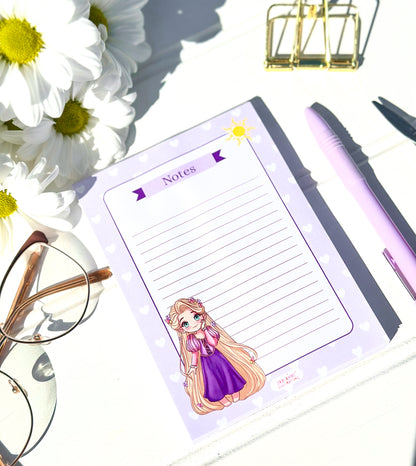 Notepad with princess rapunzel character, pen, glasses, and flowers on a white surface