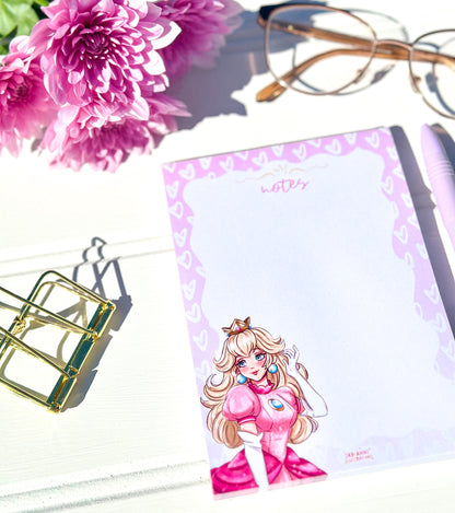 Notepad with a princess character design, pink flowers, glasses, and a pen on a white surface