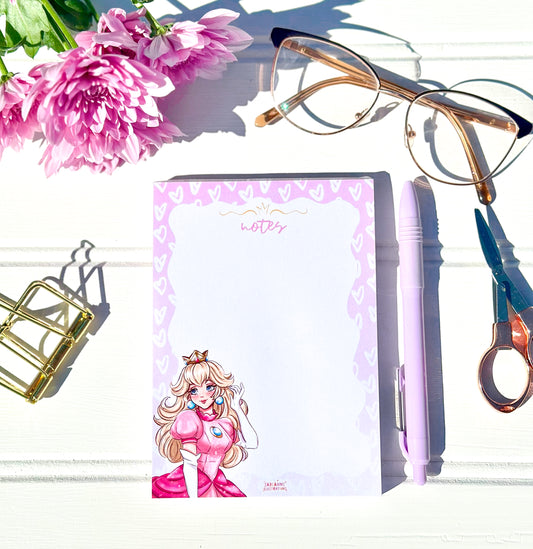 Notebook with a princess peach character design, glasses, and flowers on a white surface